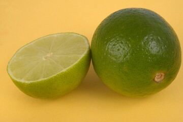 Citrons verts dont un coupé en deux en gros plan sur fond jaune