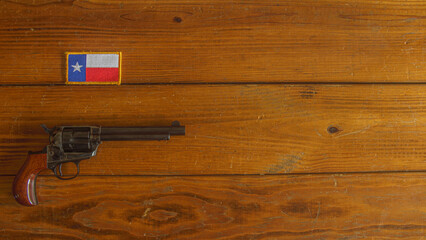 Single action revolver below a Texas state flag patch on a textured wooden plank background