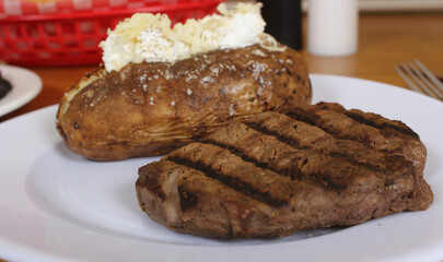 Sirloin Steak With Baked Potato and fresh rolls in background Shallow DOF Focus on Steak
