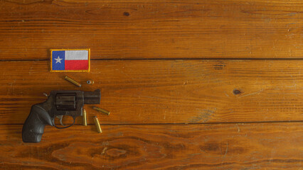 Black snub nosed revolver, with ammunition, below a Texas state flag patch on a wooden plank background