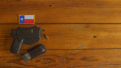semi-automatic handgun in holster, with spare magazine in a black leather carrier and ammunition, below a Texas state flag patch on a textured wooden plank background