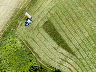 drone shot of blue tractor with mower cutting fresh green meadow somewhere in austria