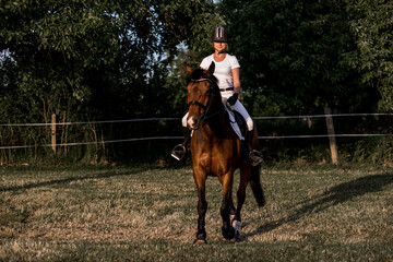 Beautiful young athlete in helmet and white sports uniform trains riding on warm summer evening ....