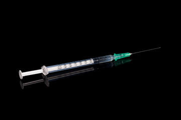 close-up of a syringe on a black shiny surface pulled up with a vaccination serum