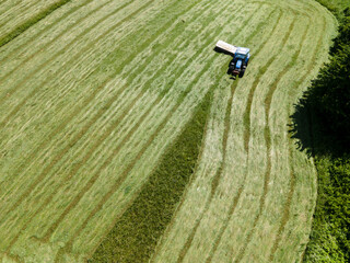 drone shot of blue tractor with mower cutting fresh green meadow somewhere in austria