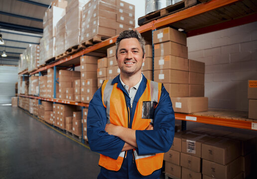 Cheerful man standing at manufacturing industry looking at camera with his arm crossed