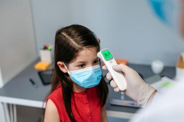 Girl without fever whose temperature is taken by her doctor with an infrared thermometer