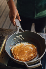making a pancake in frying pan on portable outdoor stove at campsite