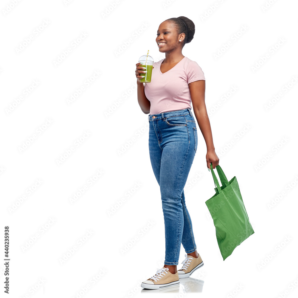 Wall mural healthy eating and sustainability concept - african american woman drinking green smoothie from plastic cup and holding reusable bag for food shopping over white background