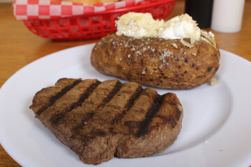 Sirloin Steak With Baked Potato and fresh rolls in background Shallow DOF Focus on Steak