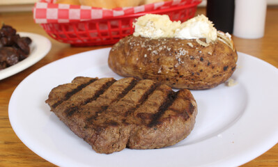 Sirloin Steak With Baked Potato and fresh rolls in background Shallow DOF Focus on Steak
