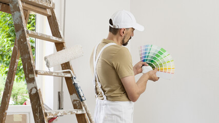 house painter man decorator choose the color using the sample swatch, work the white wall of the...