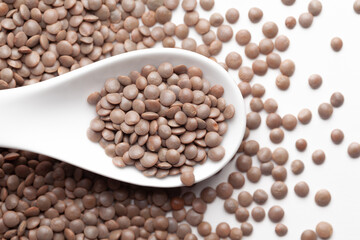 Macro Close up of Organic masoor dal (Lens culinaris) or whole brown dal on a white ceramic soup spoon. Top view,  over gradient background of itself.
