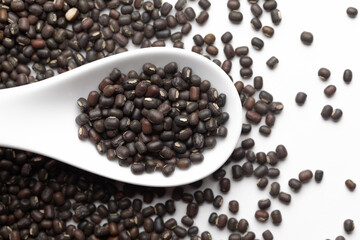 Macro Close-up of Organic Black Gram (Vigna mungo) or whole black urad on a white ceramic soup spoon. Top view,  over gradient background of itself.