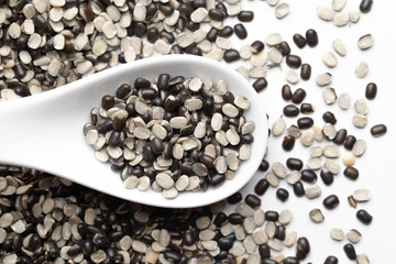 Macro Close up of Organic split black urad dal (Vigna mungo) with shell on a white ceramic soup spoon. over gradient background of itself.