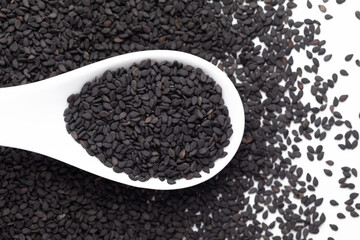 Macro Close up of Organic Black Sesame seeds(Sesamum indicum) or Black Til with the shell on a white ceramic soup spoon. Top view, over gradient background of itself.