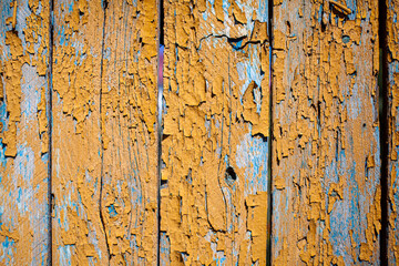 Wood texture with yellow flaked paint. Peeling paint on weathered wood. Old cracked paint pattern on rusty background. Chapped paint on an old wooden surface