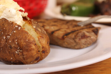 Fototapeta na wymiar Sirloin Steak With Baked Potato and fresh rolls in background Shallow DOF