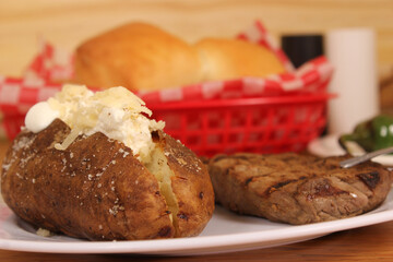 Sirloin Steak With Baked Potato and fresh rolls in background Shallow DOF