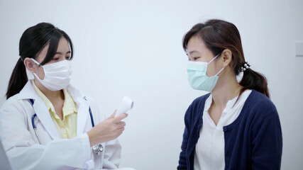 Young doctor using infrared thermometer checking body temperature of patient.