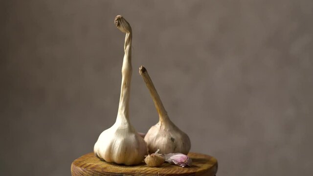 Garlic heads. Cloves of garlic on a wooden board. Dark background. Healthy vegetables. Vitamins. Rotation of the object. Close-up.