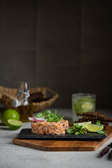Salmon fish tartare with micro greens, lime on black stone plate, dark background. Grey textured table, healthy sea food concept. Macro shot with copy space.