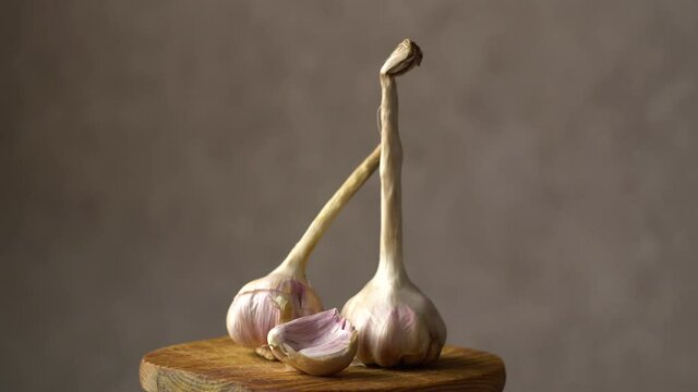 Garlic heads. Cloves of garlic on a wooden board. Dark background. Healthy vegetables. Vitamins. Rotation of the object. Close-up.