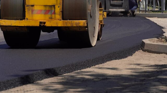 Compactor is driving over freshly poured asphalt and compresses it on the road to fix a hole. Close-up of road roller that rolls new hot asphalt. A layer of freshly laid asphalt. Road surface repair.