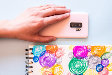 Top view of a hand picking up a phone next a paper with colorful swirls