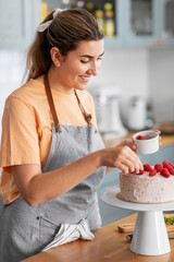 culinary, baking and cooking food concept - happy smiling young woman decorating cake with...