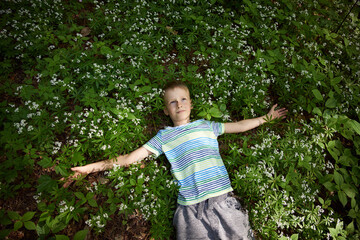 Naklejka na ściany i meble Boy 9 years old lies in the grass with flowers