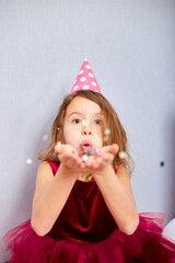 Beautiful little girl blows up multicolored confetti, having fun at home birthday party