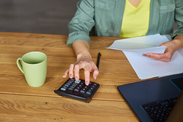 Close up of woman sit calculate expenses on calculator at wooden table, modern workplace, freelancer working