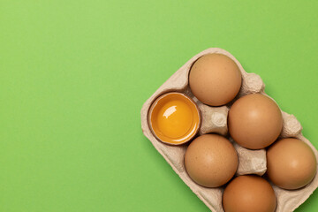 Brown chicken eggs and one broken egg with yolk in eco basket on green background