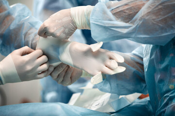 Fototapeta premium Nurses helping the surgeon to put on a glove in the operating room, many doctors' hands in gloves. Washing gloves, part of the equipment of surgeons.
