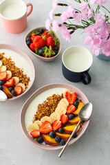 Delicious healthy breakfast, granola with yogurt and sweet fruits, banana and strawberries, blueberries and peaches, milk in a mug and flowers in a vase, top view