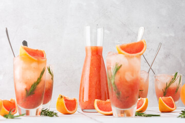 Cold refreshing grapefruit smoothie with rosemary and ice in glasses, grapefruit wedges and rosemary sprigs on the table, home party