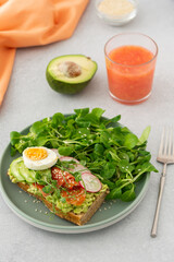 Healthy delicious breakfast, sandwich with avocado and salmon, cucumbers and radishes and microgreens of peas with boiled egg and corn salad, grapefruit smoothie in a glass