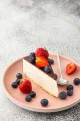 A piece of cheesecake covered with chocolate with blueberries and strawberries close-up on a pink plate with a dessert spoon