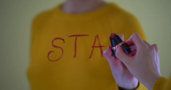 Beautiful female hand is writing START. The word START written in red lipstick on the window, romantic relationship, cute Valentines day video card. The window is decorated with a garland of