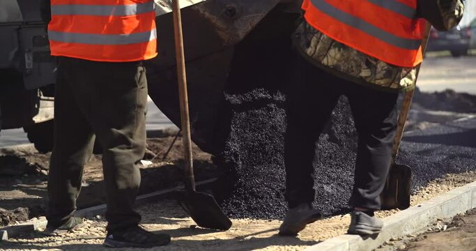 Two road workers pour hot asphalt into a paver at sunset. Road construction machines. Road repair. Beautiful sun glare.