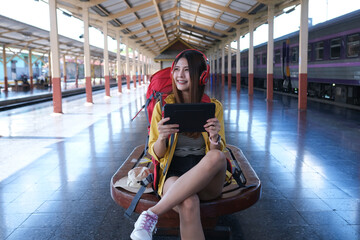 Asian traveller play her tablet and listen music for wait to start journey by train, traveling...
