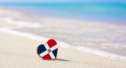 Flag of the Dominican Republic in the shape of a heart on a sandy beach. The concept of the best vacation in Dominican Republic