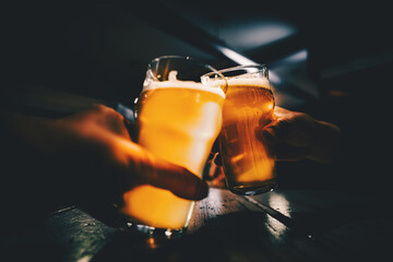 Closeup view of a two glass of beer in hand. Beer glasses clinking in bar or pub