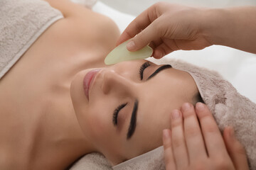 Obraz na płótnie Canvas Young woman receiving facial massage with gua sha tool in beauty salon