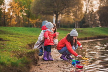 Children play with boats on the river bank. sunny autumn. yellow park. blue river at sunset
