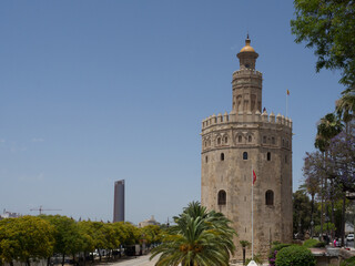 Fototapeta na wymiar View of the Torre Sevilla (the city's first skyscraper) and the Torre del Oro (Tower of Gold) with palm tree and blue sky