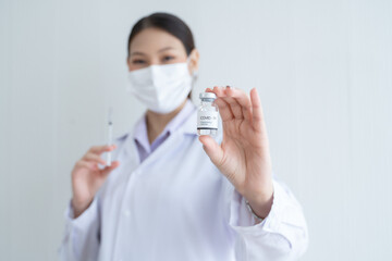 Selective focus on Covid-19 vaccines vial bottle in hand of Asian young scientist woman wear face...