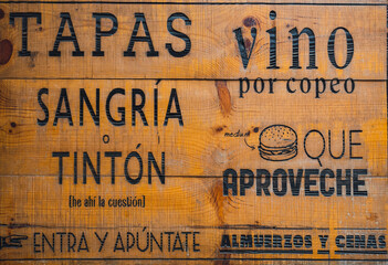 Wooden sign of a restaurant that offers lunch and dinner and that invites you to enter. In Spanish it says: Tapas, sangria, wine cup