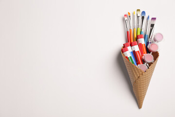 Waffle cone with different paints and brushes on white background, top view. Space for text